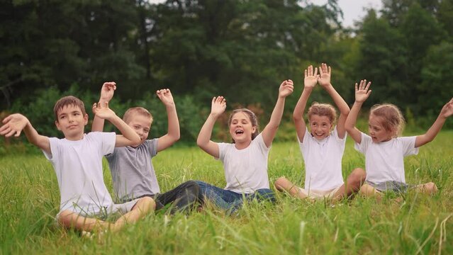 children sit on the grass in the park with their hands up. happy family childhood dream concept. kids are resting in a park in the meadow sitting on the lifestyle grass and stretching their hands up