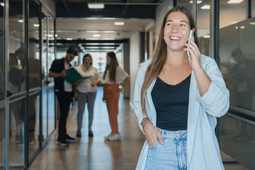 Smiling caucasian woman talking on mobile phone at a coworking space with peers behind