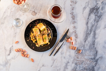 Traditional famous Turkish dessert baklava, pistachios and tea glass in black plate on marble background