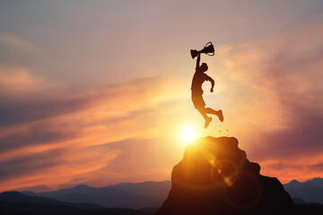 Silhouette of a businessman jumps holding a trophy on top mountain with light sunset. concept of a successful business or determination to lead the organization to success. - obrazy, fototapety, plakaty