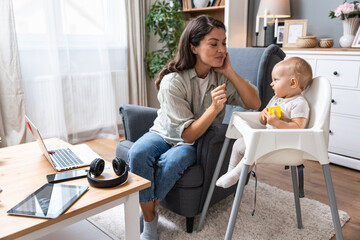 Mom and businesswoman working with laptop computer at home and playing with her baby. Female on maternity leave remotely work from home office trying to quiet down her baby.