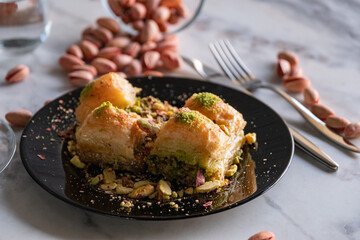 Traditional famous Turkish dessert baklava, pistachios and tea glass in black plate on marble background
