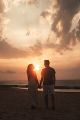 Rear view silhouettes of perfect couple in love together holding hands at tropic sea sunset. Man and woman posing walking on seascape outdoors. Summer vacation lifestyle concept. Copy ad text space