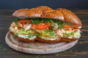 Challah Sandwich with grilled salmon, boiled potato, cream cheese, fresh tomatoes and herbs over wooden background.