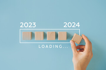 Female hand putting wooden cube for countdown to 2024. Loading year from 2023 to 2024. New year...