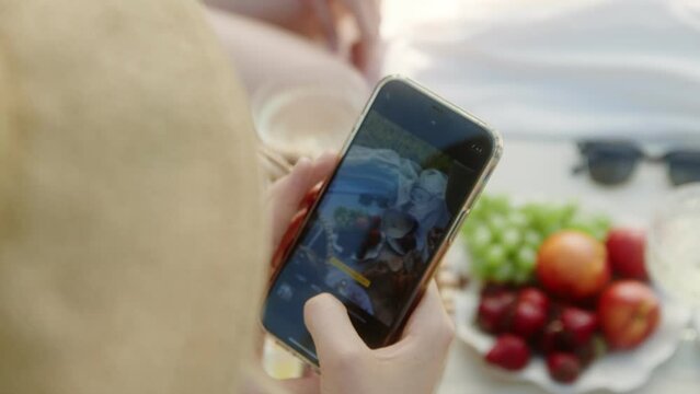 A woman's hand takes pictures of fruits and vegetables on a picnic on her phone