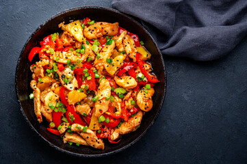 Stir fry chicken with pineapple, red paprika, chives, soy sauce and sesame seeds in frying pan. Asian cuisine dish. Black table background, top view