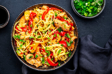 Stir fry noodles with chicken slices, pineapple, red paprika, chives, soy sauce and sesame seeds in ceramic bowl. Asian cuisine dish. Black table background, top view