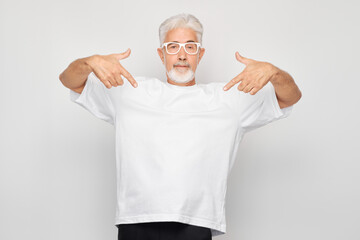 Gray-haired mature man 60 years old in white T-shirt pointing finger down, demonstrating empty...