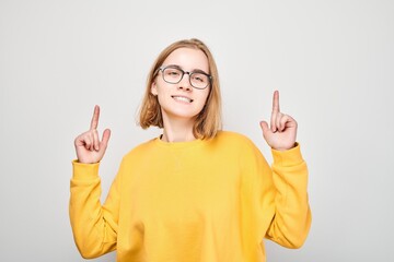 Young blond girl in yellow casual pointing up finger, demonstrating empty space for product or text isolated on white studio background.