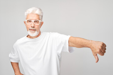 Portrait of elderly gray-haired man showing thumbs down isolated on white studio background....