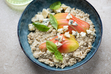 Risotto with pear, blue cheese and fresh basil in a blue bowl, horizontal shot on a beige stone surface, middle close-up