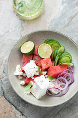 Plate of salad with watermelon, feta cheese, cucumber and red onion, vertical shot on a grey granite background, elevated view