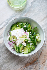 Bowl of fresh cucumber and feta cheese salad on a light-grey granite background, vertical shot