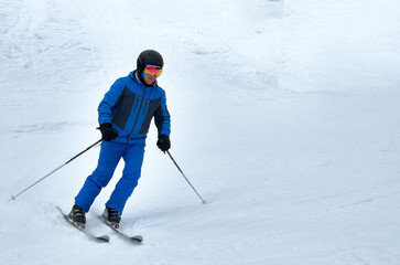 A man in blue sportswear on skis rides down a snowy slope