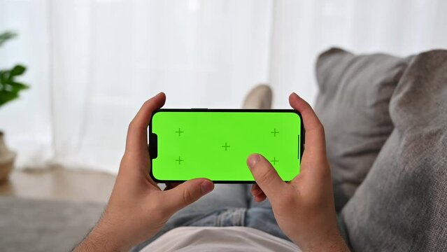 Closeup of man using smartphone with green screen tapping on the screen. Mobile games ,social media, etc