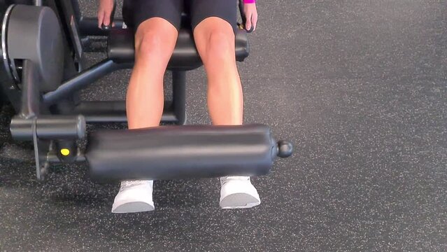 Girl does exercises in gym and does leg extension training on simulator. Sports fitness press and legs triceps