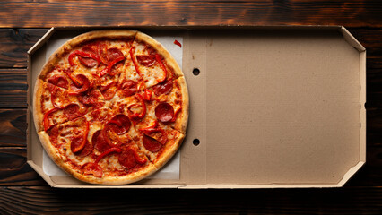 Pepperoni pizza with bell peppers in open carton box on dark wooden table flat lay with copy-space