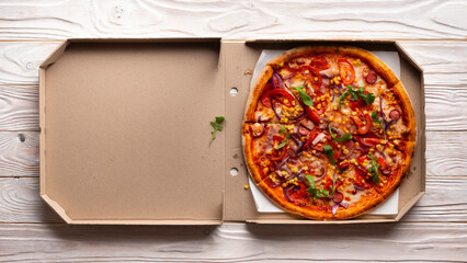 Pepperoni pizza with bell peppers sweetcorn and arugula in open carton box on white wooden kitchen...