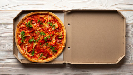 Pepperoni pizza with bell peppers and arugula in open carton box on white wooden kitchen table flat...