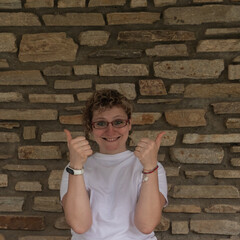 Young Woman in T-shirt and Glasses Showing Approval near Rustic Brick Wall