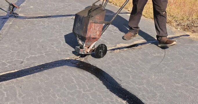 In course of worker patching patcher performs coated crack filling asphalt crack sealing bitumen emulsion road surface restoration