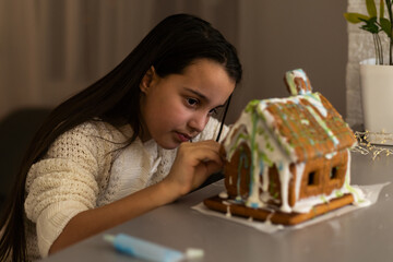 gingerbread house. little girl in holidays preparations putting glazing on gingerbread house Christmas trees.