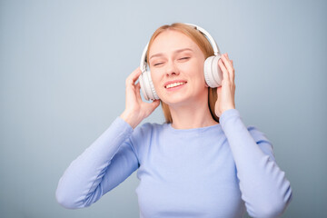 Happy girl listening to music through wireless headphones on blue background. Portrait of a young woman wearing headphones with space for text.
