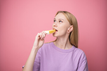 Happy young woman eating yellow ice cream on pink background. Concept of summer and sweet cold desserts.