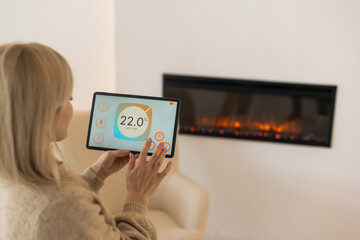 Holding digital tablet in cozy living room with fireplace on background. smart home app