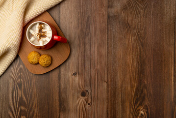 Mug of hot chocolate and cookies with soft winter scarf on wooden background. Top view