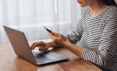 Searching for information on the Internet on the phone. A girl works with a smartphone and a laptop on a table