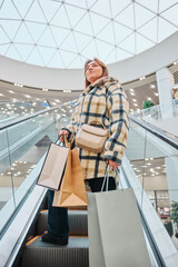 woman shopping in mall, a woman on an escalator in a shopping mall with paper bags