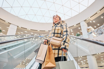 woman shopping in mall, a woman on an escalator in a shopping mall with paper bags