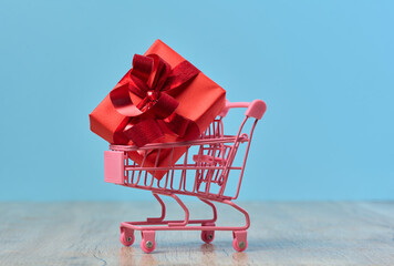A gift wrapped in red paper in a miniature shopping cart on a blue background