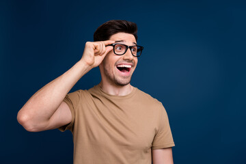 Photo of attractive excited man wear trendy clothes hold glasses look empty space offer news banner isolated on dark blue color background