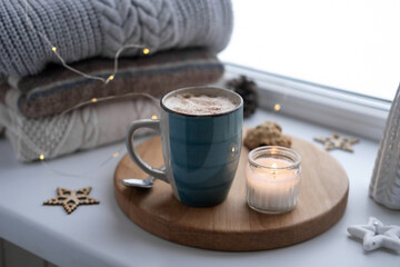Winter windowsill still life. Blue ceramic cup of hot coffee on window sill. Christmas decorations...