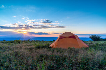 Sunrays warmly shine over a peaceful campsite at the edge of a mountain meadow.