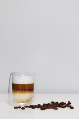 close up of glass of fresh latte coffee with coffee beans on white table and copy space