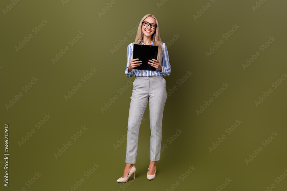 Wall mural Full body photo of blonde attractive young woman papers look empty space dressed stylish striped clothes isolated on khaki color background