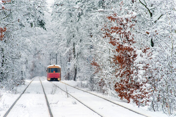Old red tram, leaving the distance through the snow-covered forest. Selective focus.