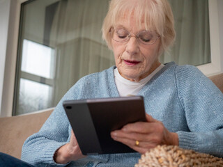 An 80 year old lady sitting using her Tablet for online shopping.