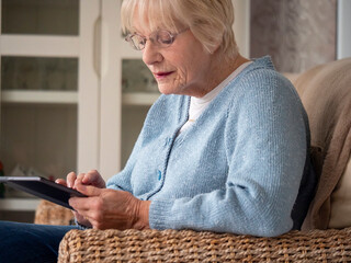 An 80 year old lady sitting using her Tablet for online shopping.