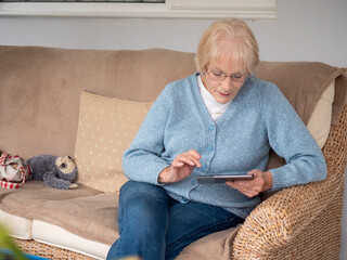 An 80 year old lady sitting using her Tablet for online shopping.