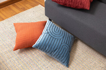 Modern and luxury pillow lying on carpet and sofa in living room. Blue, red, and orange pillow in...