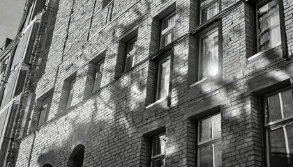 black and white abstraction of sunlight reflecting on brick building facade with windows in shadow