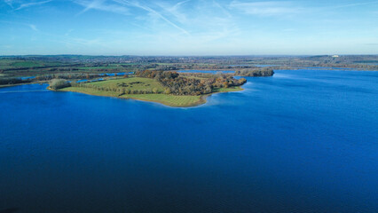 Aerial view 4k wide angle of fields and Rutland water, England, cloudy skies and green patches of forest.