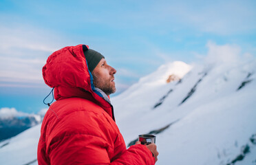 Portrait of high altitude mountaineer dressed red warm dawn jacket holding metal mug of hot tea...