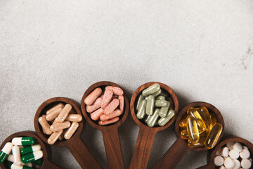 Vitamins and supplements. Variety of vitamin tablets in wooden spoons on a texture background. Multivitamin complex for every day. Nutritional supplements. Place for text. Copy space.