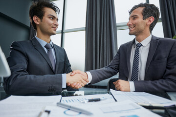 Fototapeta premium Smiling businessman shaking client hand, closing successful deal, sitting at table in office